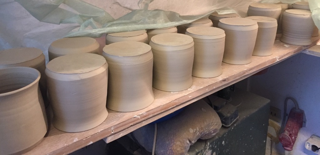 Unfired ceramic lidded jars drying under plastic sheeting in the studio