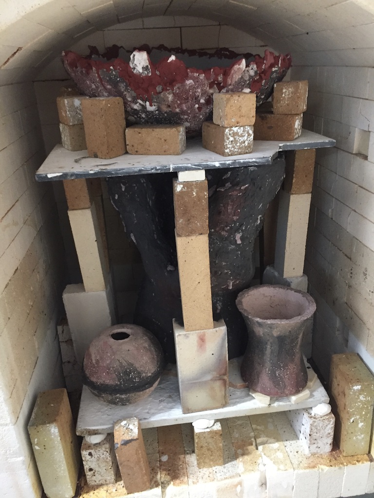 Kiln interior showing a dramatic red-glazed bowl and ceramic forms on kiln shelves
