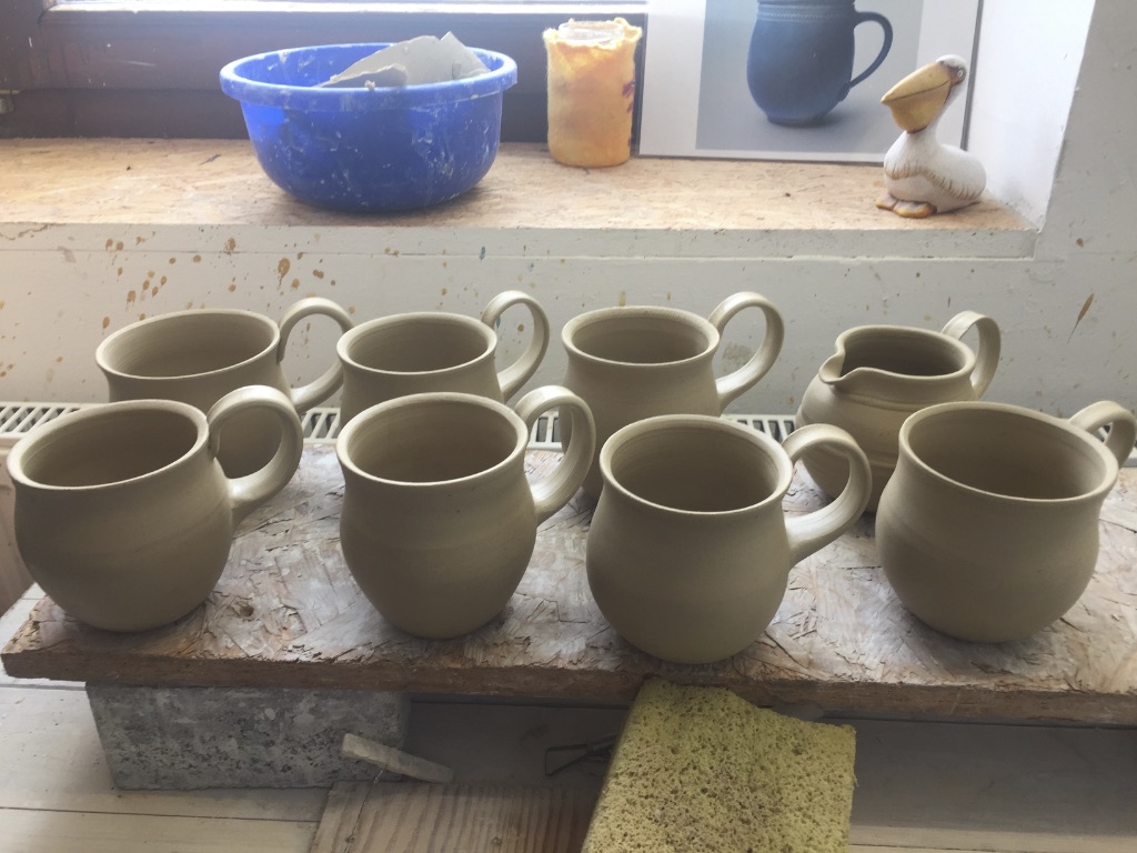 Unfired stoneware mugs and pitcher drying on a board in Catharina Goldnau studio